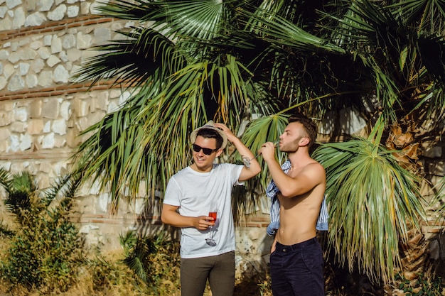 Dos amigos, hombres jóvenes con copas de champán en el fondo de vegetación tropical.
