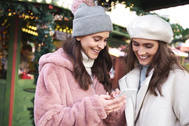 Dos amigos en un mercado de Navidad navegando por teléfono móvil