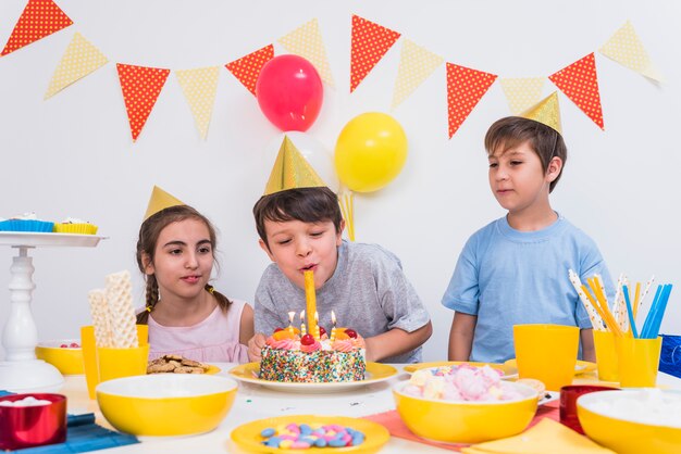 Dos amigos mirando al niño soplando las velas en el pastel de cumpleaños