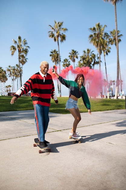 Dos amigos montando sus patinetas con una bomba de humo afuera en el parque