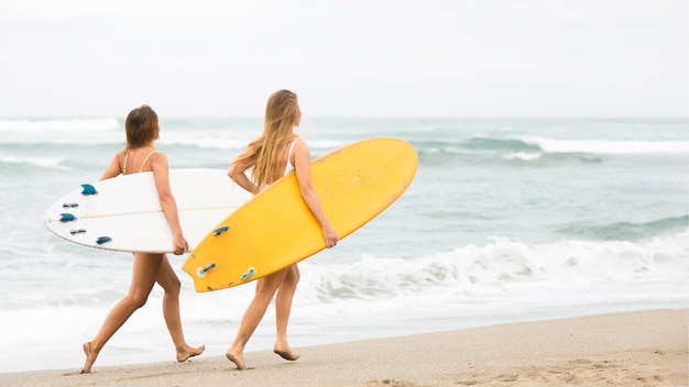 Foto gratuita dos amigos sonrientes corriendo en la playa con tablas de surf