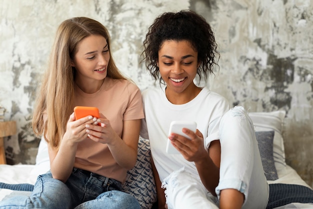 Dos amigos sonrientes en sus teléfonos inteligentes en la cama