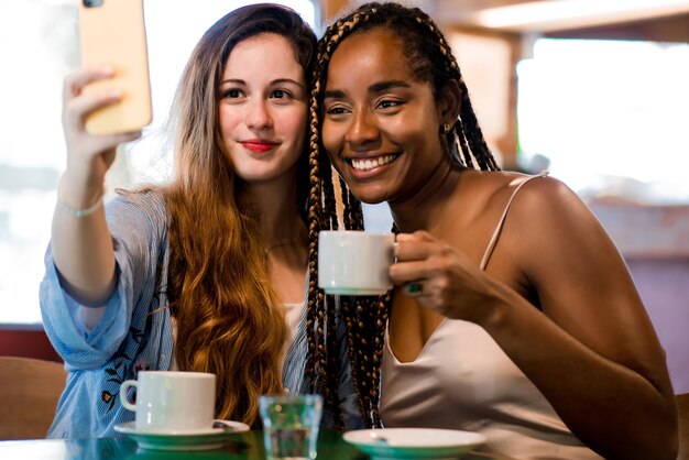 Dos amigos tomando un selfie con teléfono móvil mientras beben una taza de café en una cafetería. Concepto de amigos.