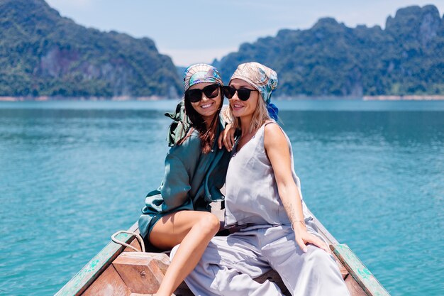 Dos amigos turísticos blogger de mujer feliz en traje de seda y bufanda y gafas de sol de vacaciones viajan por Tailandia en barco asiático, Parque Nacional Khao Sok.