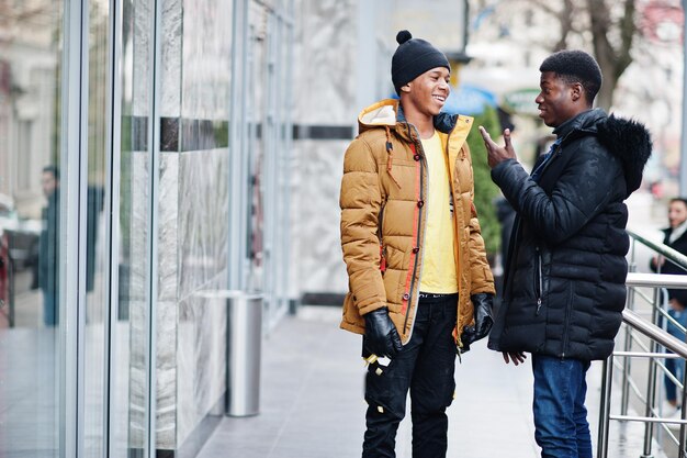 Dos amigos varones africanos hablando juntos usan chaquetas en clima frío