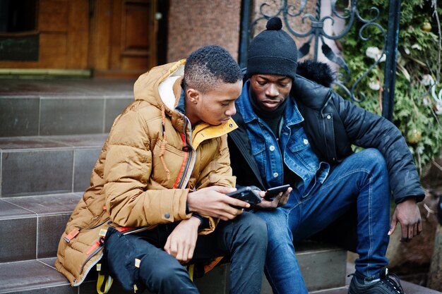 Dos amigos varones africanos sentados y mirando juntos por teléfono