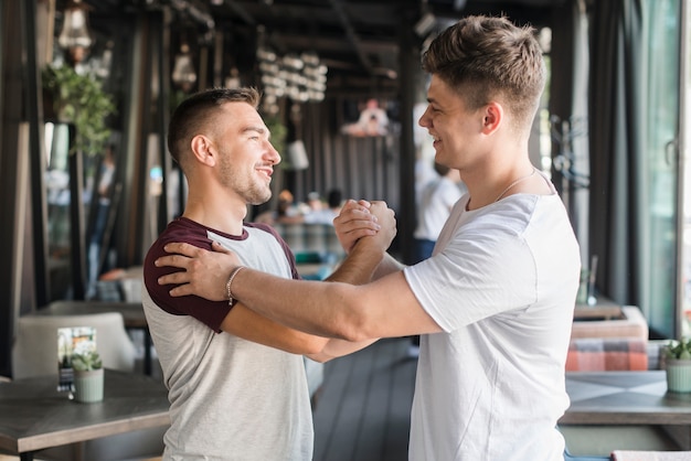 Dos amigos varones jóvenes felices estrechándole la mano en el restaurante