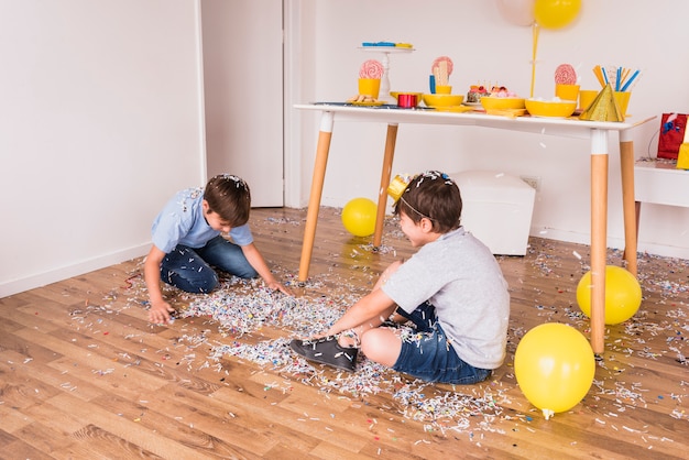 Dos amigos varones jugando con confeti en fiesta en casa