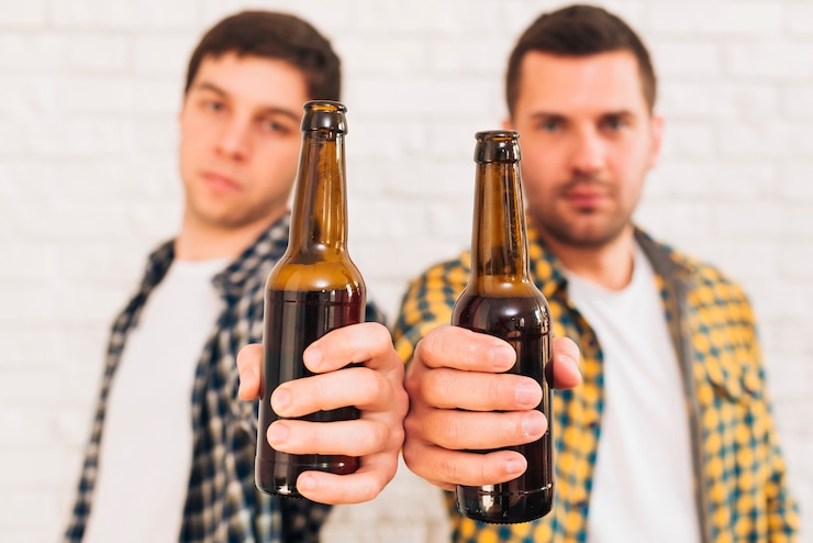 Foto gratuito dos amigos varones de pie contra la pared de ladrillo blanco que muestra botellas de cerveza hacia la cámara