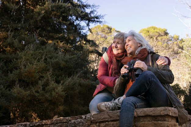 Dos ancianas disfrutando de una caminata en la naturaleza mientras usan binoculares