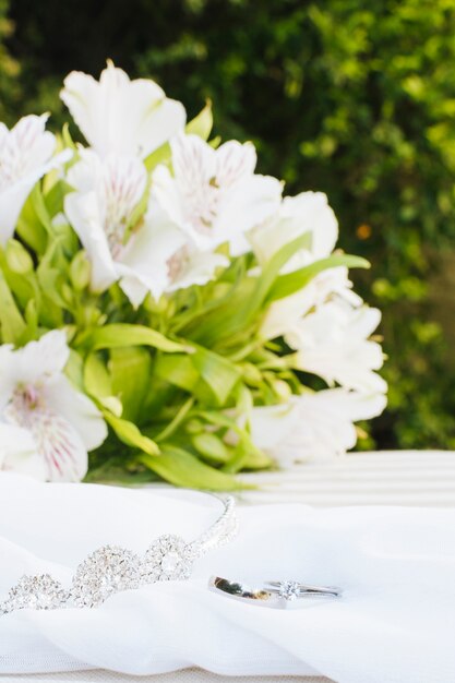 Dos anillos de boda y una corona en la bufanda con un hermoso ramo de flores sobre la mesa