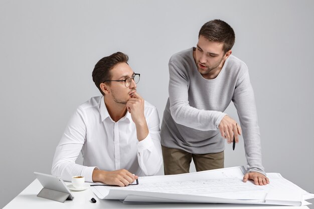 Dos arquitectos discuten el proyecto de construcción. Hombre joven sin experiencia pide consejo