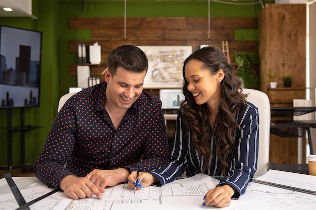 Dos arquitectos sonrientes se sientan en una mesa y discuten un nuevo proyecto. Oficina moderna y blue print