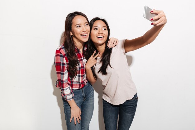 Dos asiáticas alegres positivas damas hermanas hacen selfie