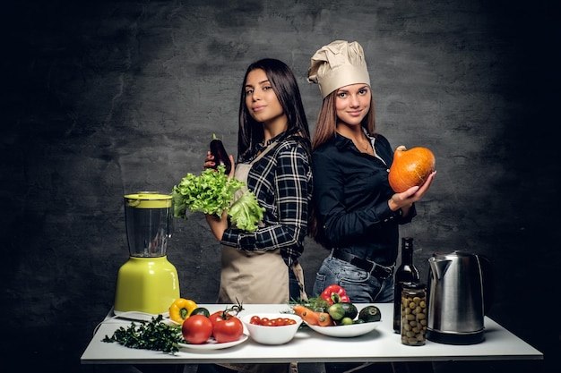 Foto gratuita dos atractivas chefs comienzan a preparar jugo de vegetales en una licuadora.