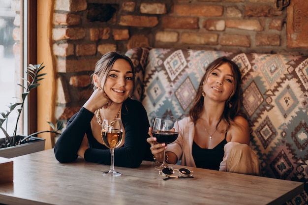 Dos atractivas chicas sentadas en un café y bebiendo vino