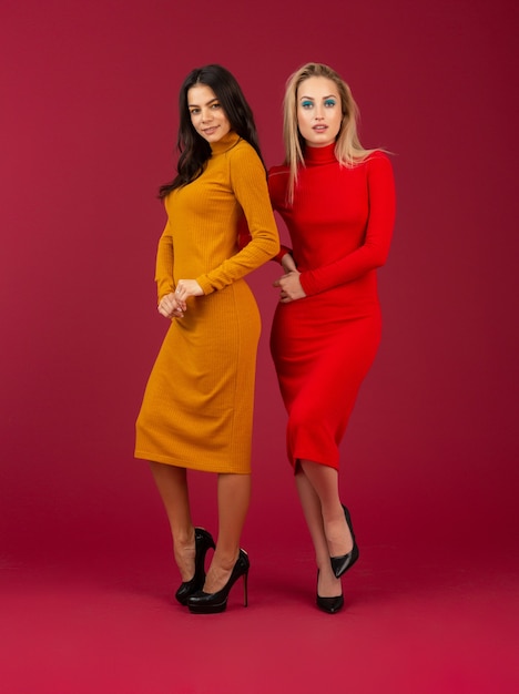 Dos atractivas mujeres con estilo en amarillo y rojo otoño invierno vestido de punto de moda posando aislado en la pared roja