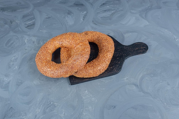 Foto gratuita dos bagels cubiertos de sésamo sobre una tabla de madera negra sobre superficie de mármol.