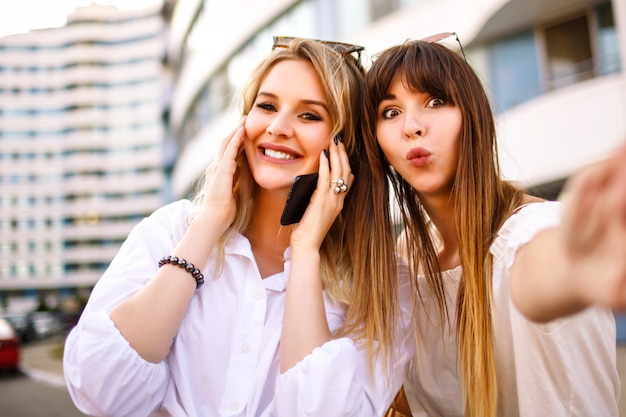 Dos bastante rubia varita mujer habilidades positivas hermanas mujer haciendo selfie en la calle, colores soleados de verano, camisas blancas salieron de emociones.