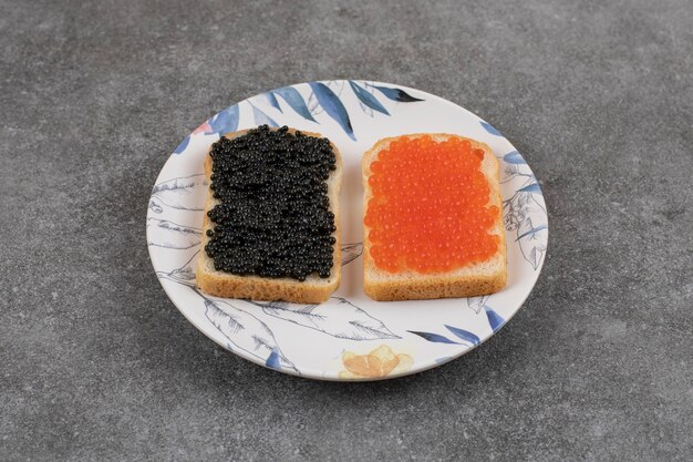 Dos bocadillos frescos con caviar rojo y negro en placa sobre superficie gris