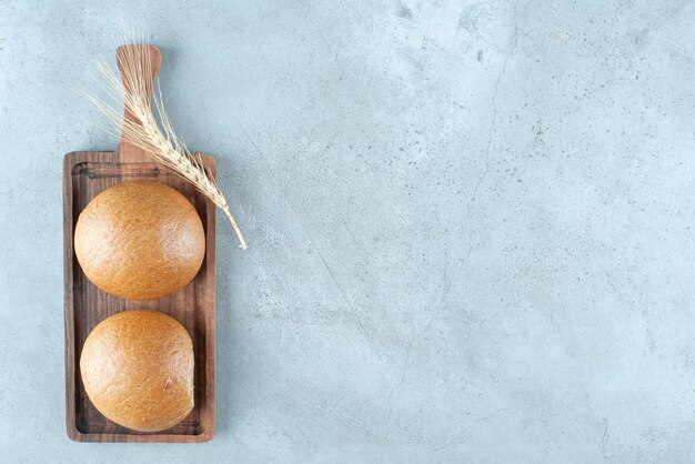 Dos bollos frescos sobre tabla de madera con trigo.