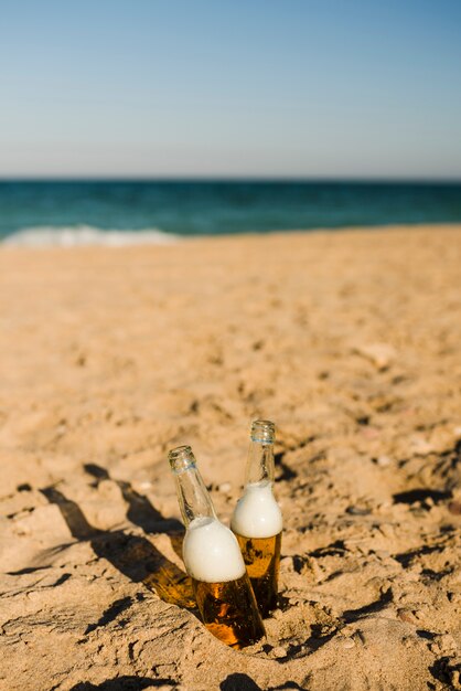 Dos botellas de cerveza helada en la arena bajo el sol brillante en la playa