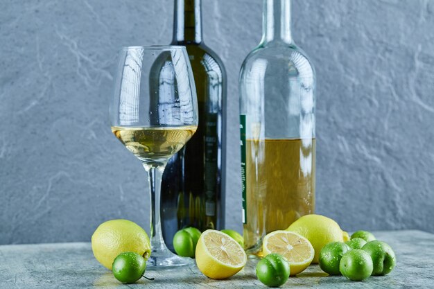 Dos botellas y una copa de vino en la mesa de mármol con limones y ciruelas cereza