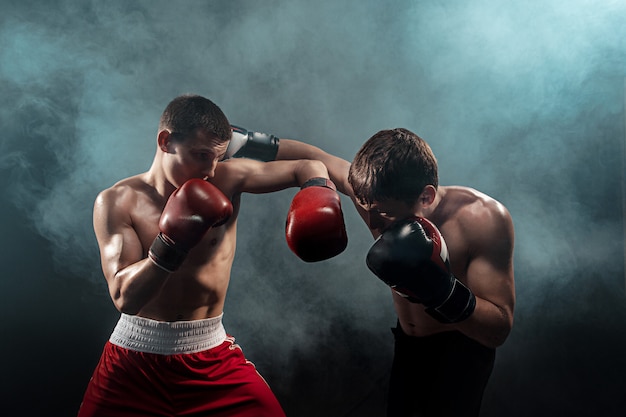 Foto gratuita dos boxeadores profesionales sobre fondo negro ahumado,