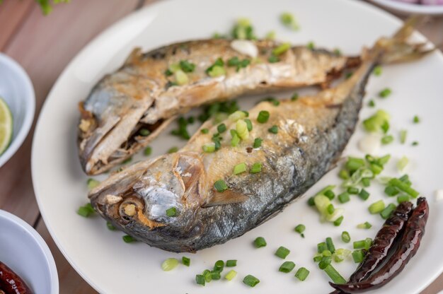 Dos caballas cocidas, colocadas en un plato blanco, espolvoreadas con cebolletas.