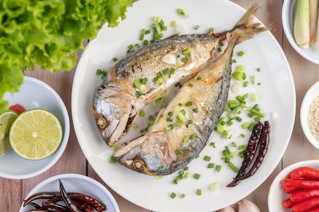 Dos caballas cocidas, colocadas en un plato blanco, espolvoreadas con cebolletas.