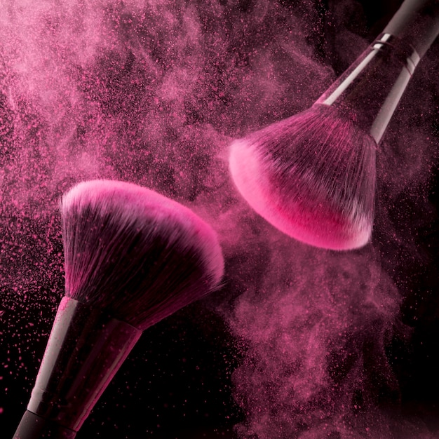 Foto gratuita dos cepillos cosméticos y polvo rosa sobre fondo oscuro