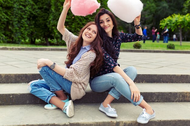 Dos chicas alegres divirtiéndose con algodón de azúcar al aire libre