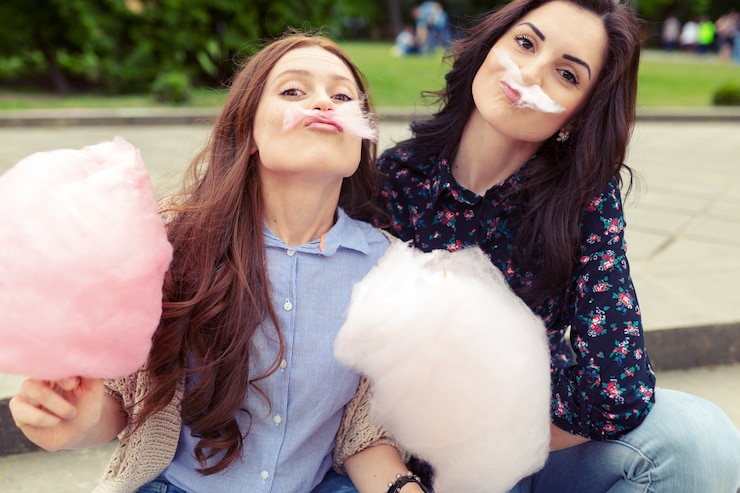 Foto gratuito dos chicas alegres divirtiéndose con algodón de azúcar al aire libre