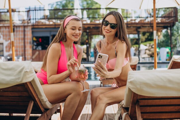 Dos chicas atractivas bebiendo cócteles junto a la piscina