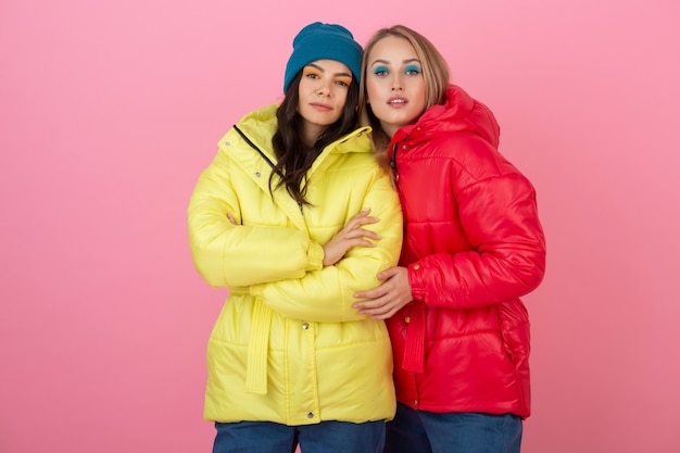 Dos chicas atractivas posando sobre fondo rosa en una colorida chaqueta de invierno de color rojo y amarillo brillante