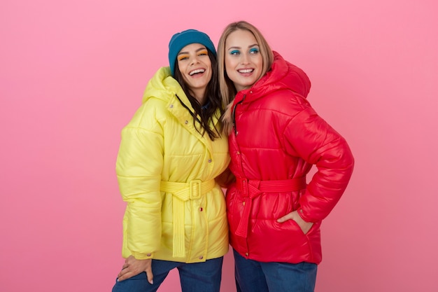 Dos chicas atractivas posando sobre fondo rosa en una colorida chaqueta de invierno de color rojo y amarillo brillante