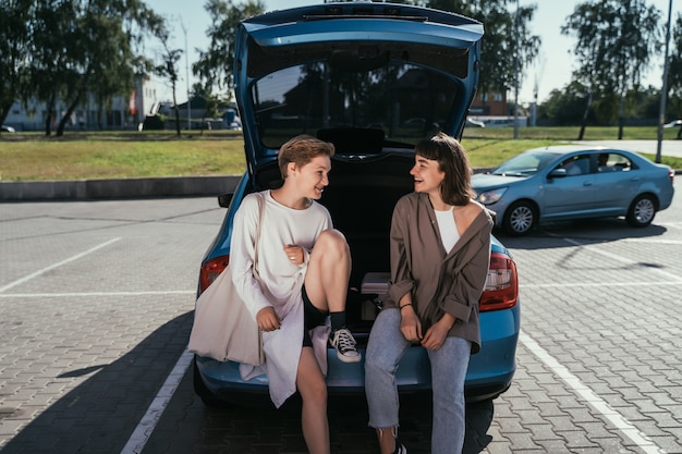 Dos chicas en el estacionamiento en el baúl abierto