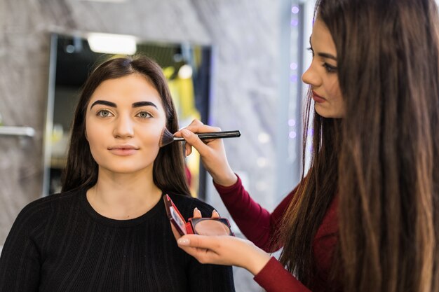 Dos chicas están trabajando en el maquillaje brillante de la noche