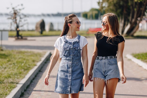 Dos chicas guapas jóvenes en un paseo por el parque. Un día soleado de verano, alegría y amistades.