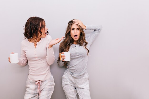 Dos chicas guapas en pijama jugando en la pared gris. Se divierten juntos.