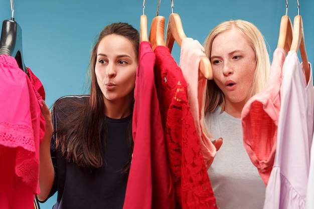 Las dos chicas guapas que miran vestidos y se lo prueban mientras eligen en la tienda