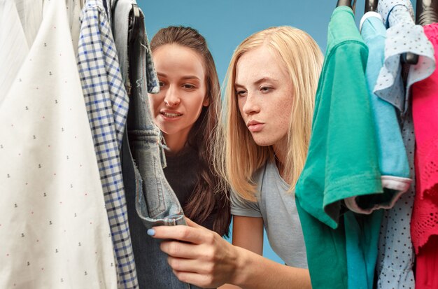 Las dos chicas guapas que miran vestidos y se lo prueban mientras eligen en la tienda