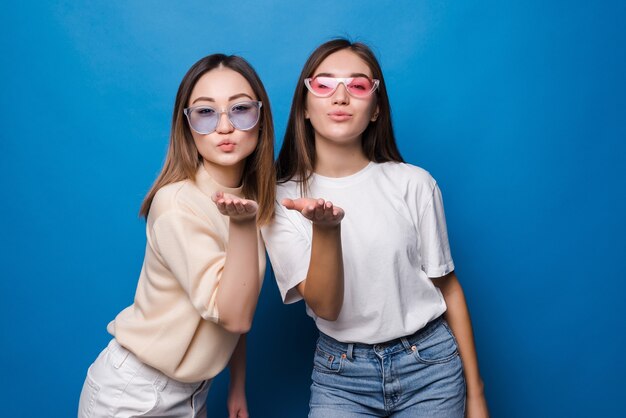 Dos chicas guapas vestidas con ropa de verano de pie y enviando un beso aislado sobre la pared azul