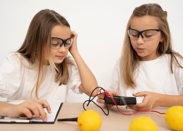 Dos chicas haciendo experimentos científicos con limones y electricidad.