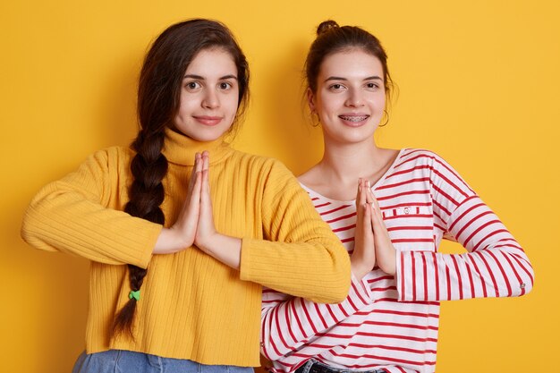 Dos chicas jóvenes con camisas casuales posando con palmeras juntas y sonrientes