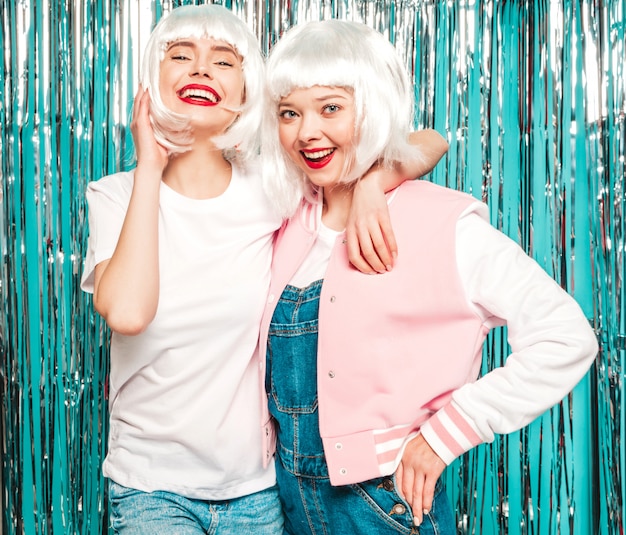 Dos chicas jóvenes hipster sexy con pelucas blancas y labios rojos. Hermosas mujeres de moda en ropa de verano verano divirtiéndose