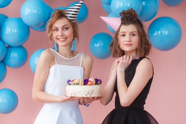 Dos chicas jóvenes que sostienen la torta de cumpleaños y muestran emociones muy emocionadas.