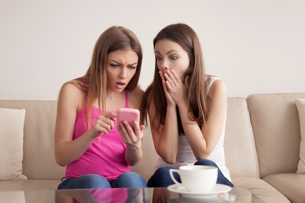 Foto gratuita dos chicas jóvenes sorprendidas mirando la pantalla del teléfono inteligente.