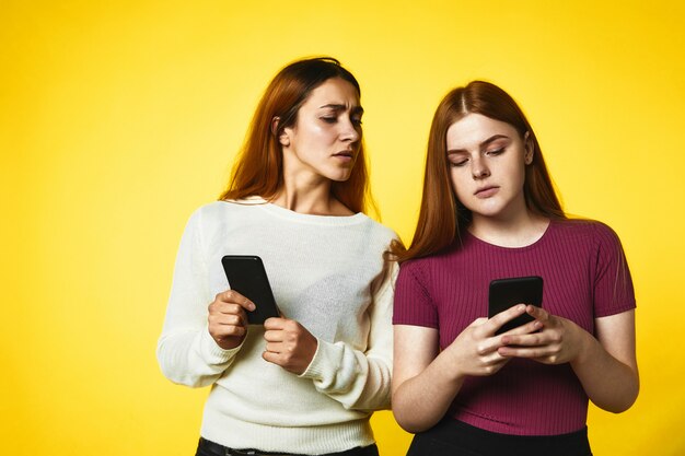 Dos chicas jóvenes sostienen teléfonos y una chica mira en el teléfono de otra chica de pie