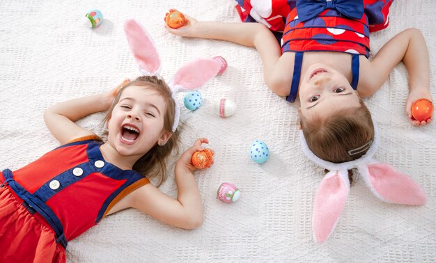 Dos chicas lindas divertidas con huevos de Pascua y orejas de conejo en un hermoso vestido brillante.